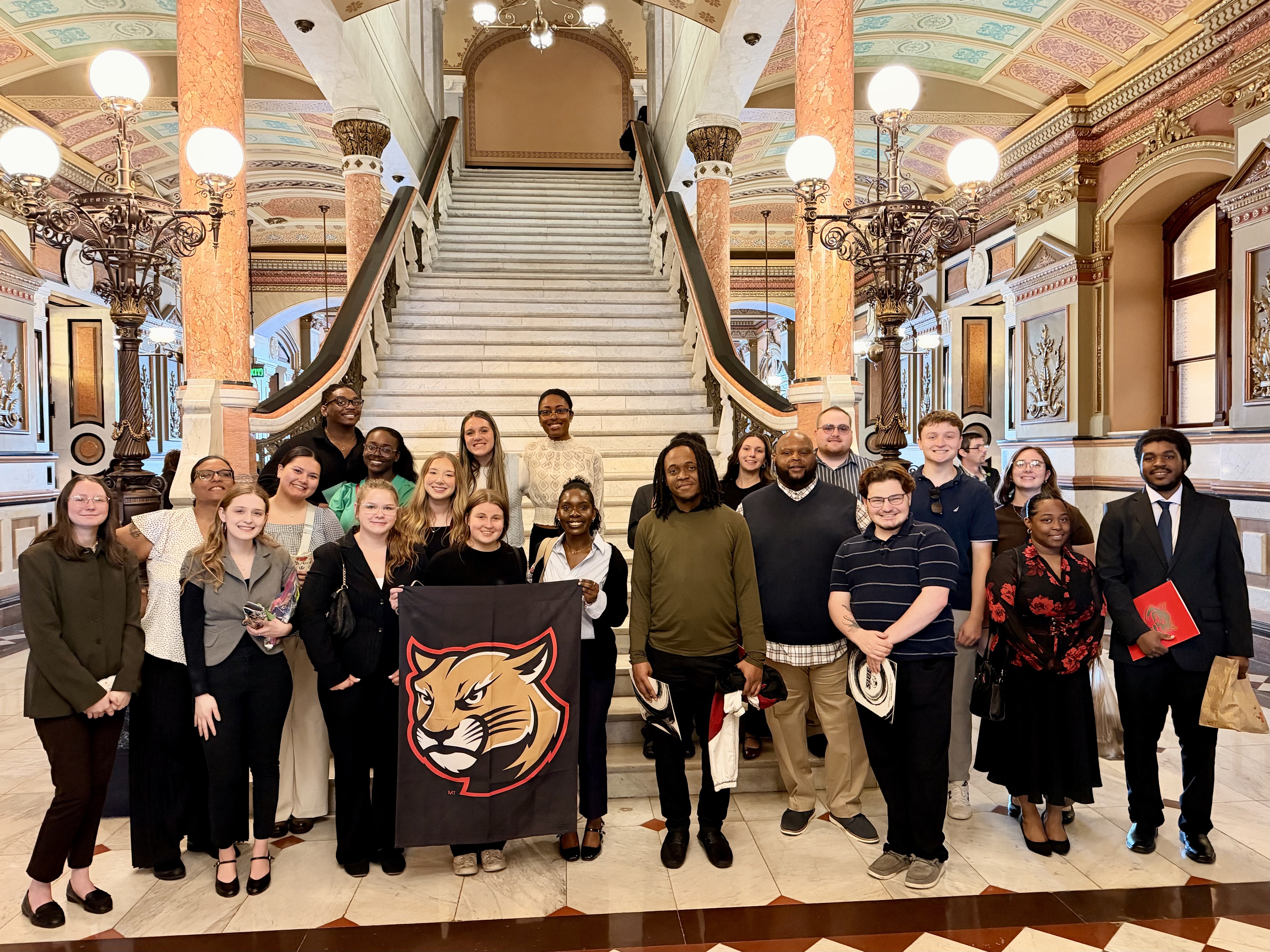 A large group of BSW students post with the Cougar banner in the Illinois Capitol