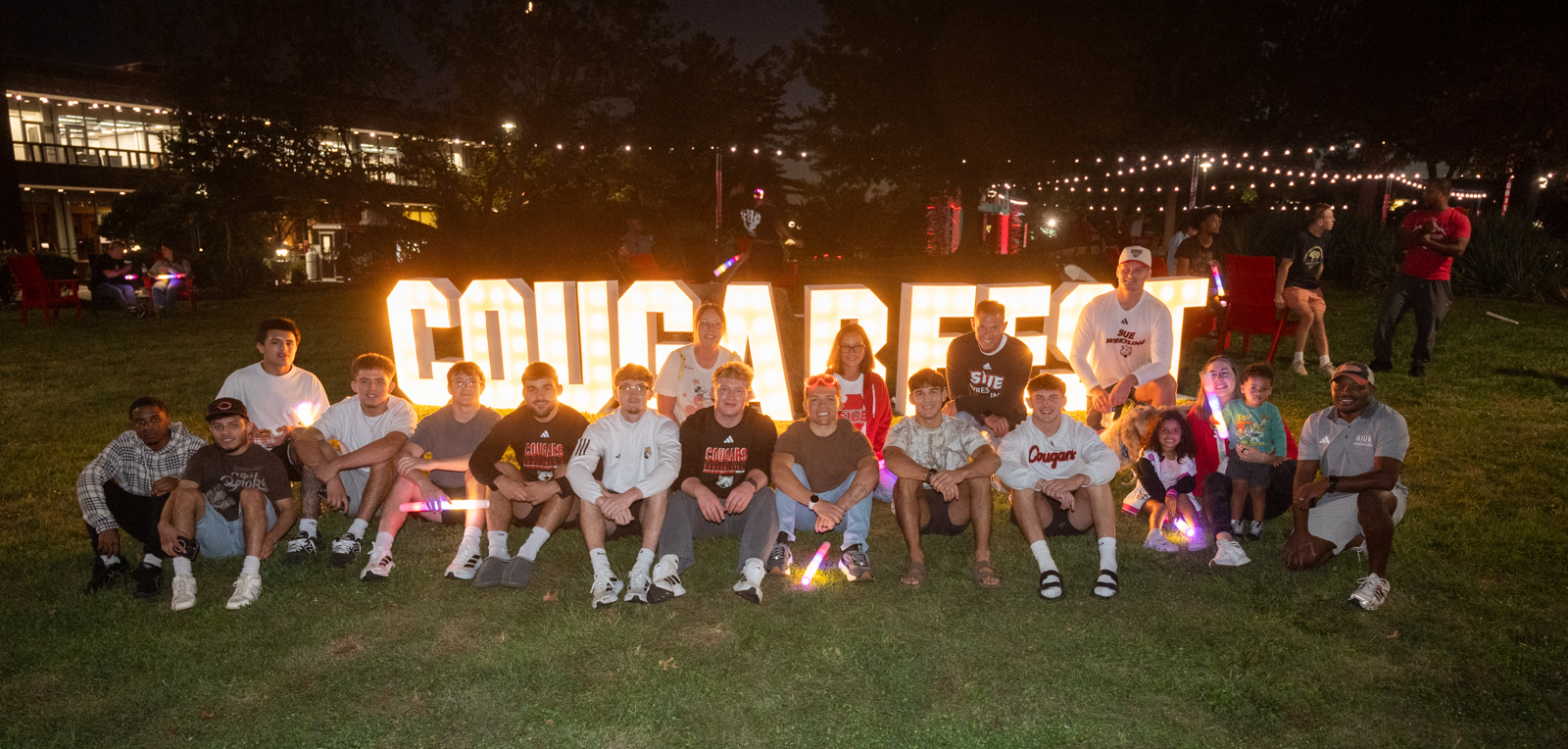 SIUE students pose with glow sticks in front of illuminated “Cougarfest” letters during the 2025 Homecoming &amp; Family Weekend celebration.