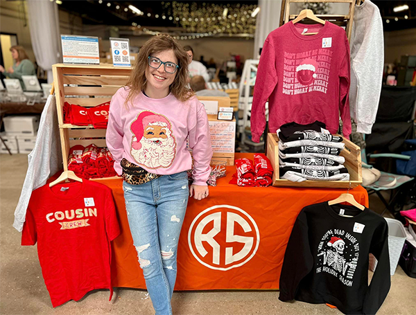 Amie Spangler standing in her store in front of display table of tees and sweatshirts
