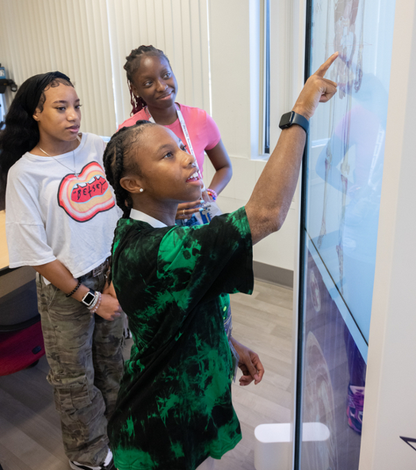 Three students standing and looking at skeleton on smart screen