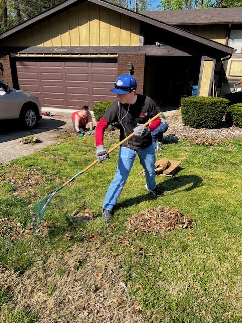 Student cleans lawn with long handled yard tool