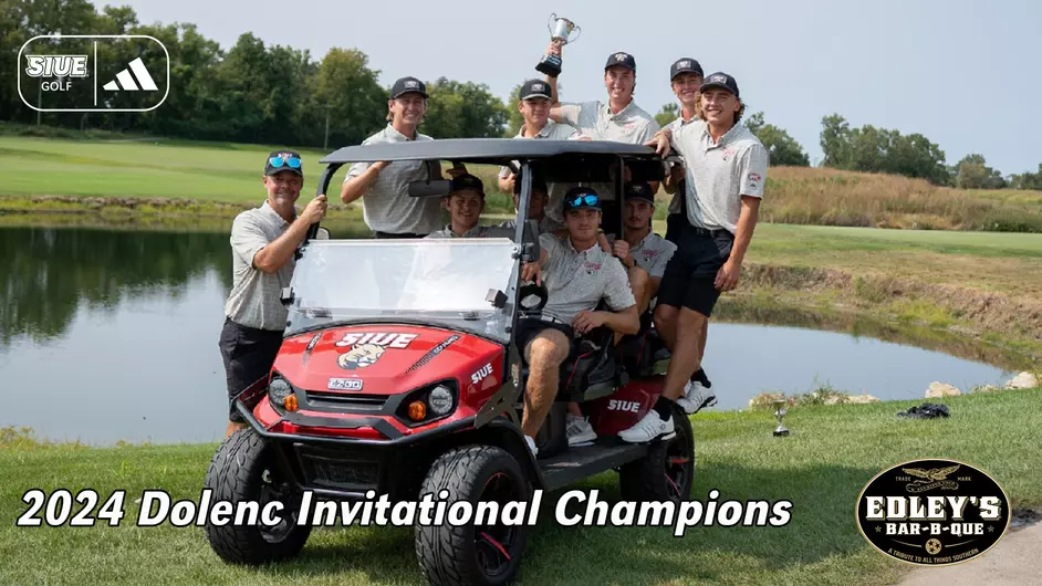 2024 SIUE mens golf team on a golf course in front of a pond on a sunny day. They are inside a large golfcart and standing on the back of it holding a cup-style trophy. There is an overlay of text reading 2024 Dolenc Invitational champions