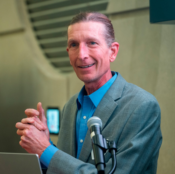 Jason Hill speaking at a podium inside the atrium of the engineering building