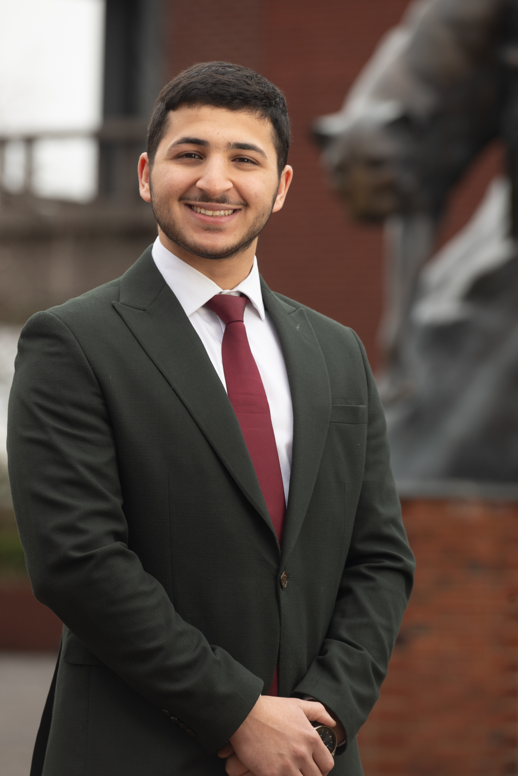 Portrait of Mo Abuzaneh wearing a suit standing outside the Cougar Statue