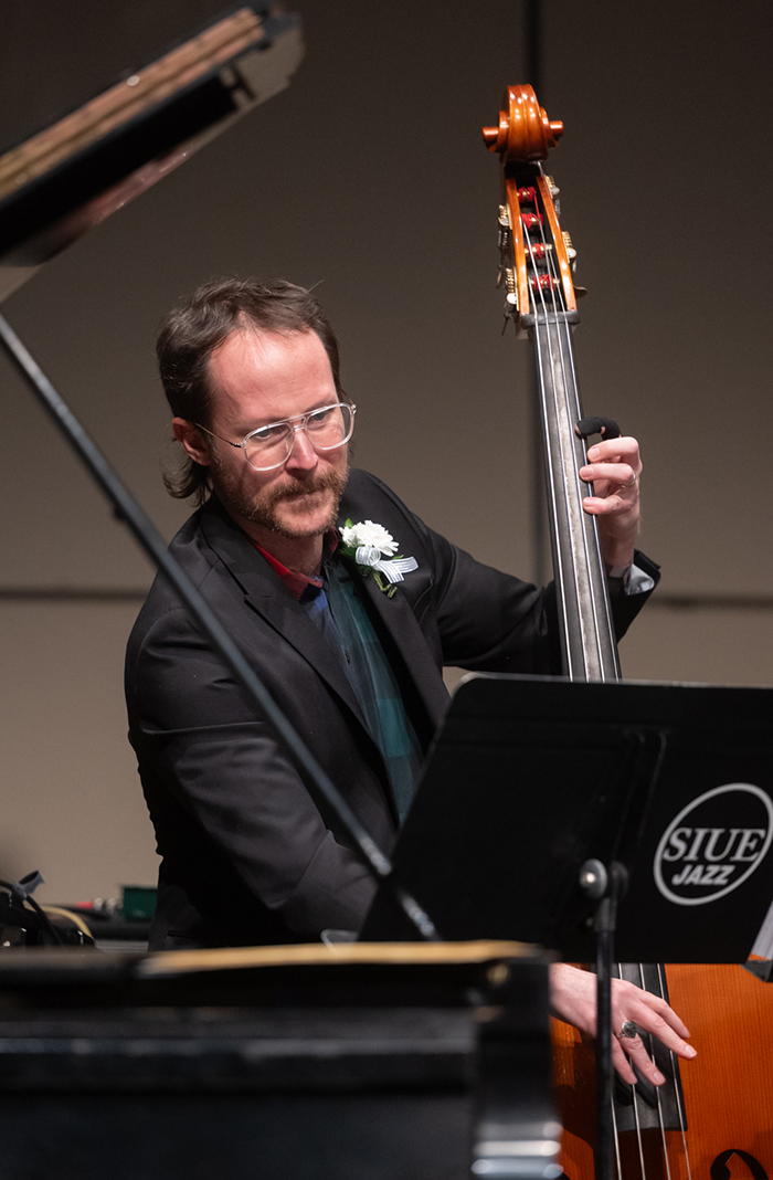 Alumnus Nick Jost playing an upright bass on stage at Katherine Dunham Theater. He is wearing a suit and boutonniere. 