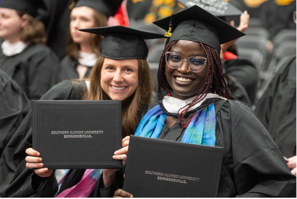 Two graduates hold diploma covers and pose for the camera