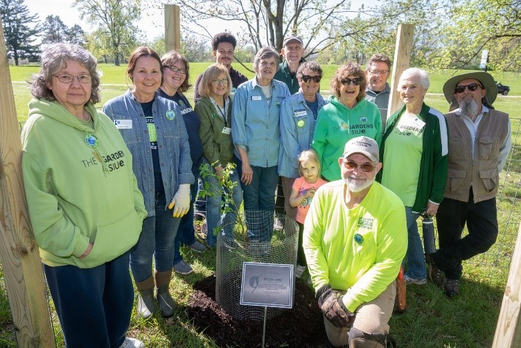 Group of 13 people and a child helping to plant the moon tree in the gardens