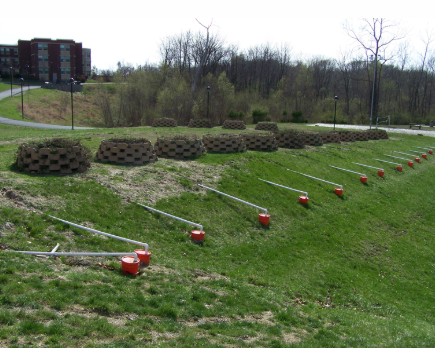 Photo of campus on the North side of Bluff Hall. There are large planters being used for a campus greenscaping project. In the background are the woods just north of Bluff Hall