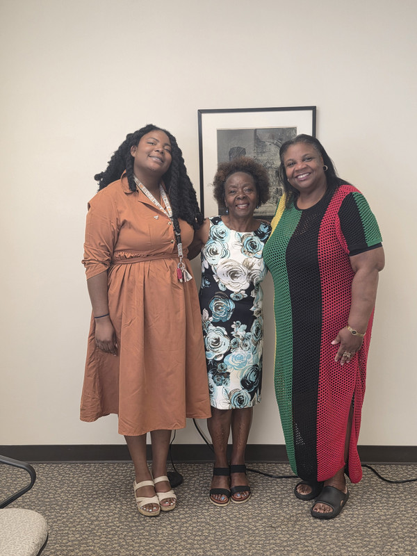 Three women pose at Juneteenth celebration and one is in dress with Juneteenth colors