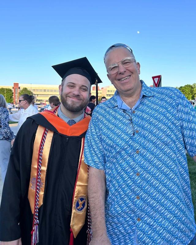 Jared at graduation in regalia with family member on a sunny day