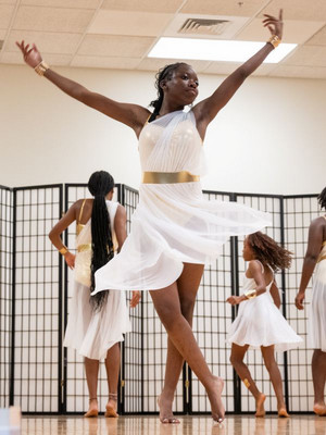 A ballet style dancer twirling in a dress elegantly in front of three other dancers 