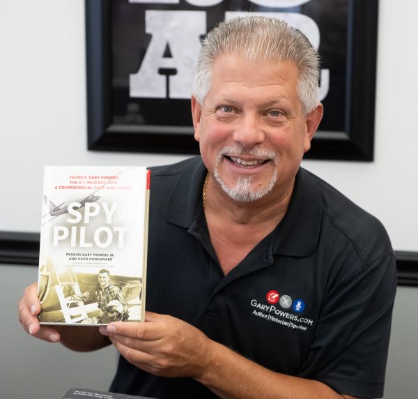 Francis Gary Powers Jr. smiling and holding a copy of his book, "Spy Pilot" in a Morris University Center Event Room