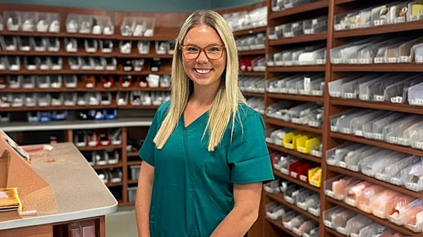 Libby Ahlers in medical scrubs stands in front of bookcases