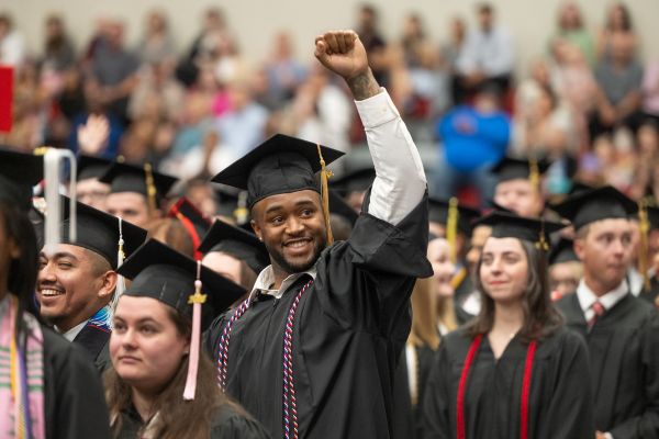Photo of SIUE graduates in regalia at a commencement ceremony. The graduate in the center of the photo has his fist pumped skyward