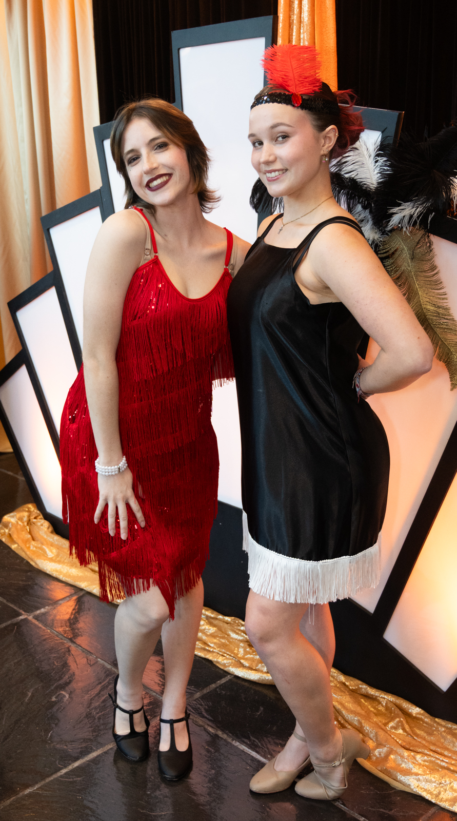 Two students dressed as 20's showgirls in front of an art nouveu structural banner decoration