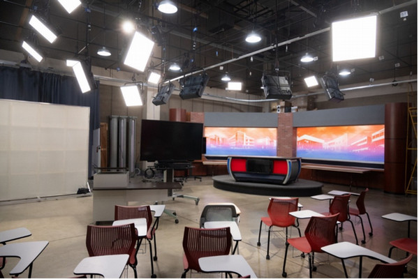 Wide studio with anchor desk monitor wall and student desks