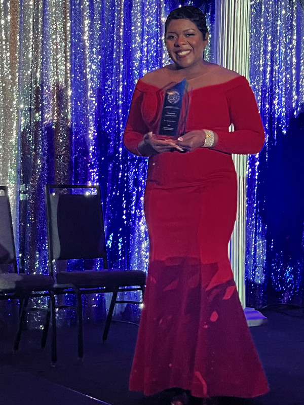 Tandra Taylor stands on stage holding award