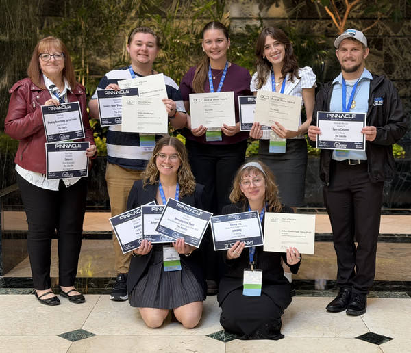 Faculty member and student journalists pose for camera with awards