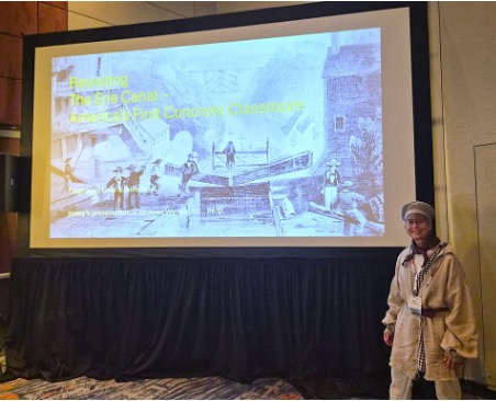 Prof stands next to a large screen projecting her presentation