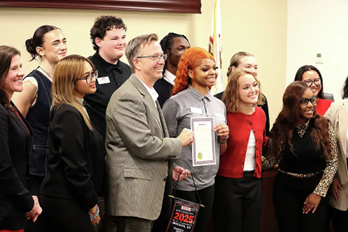 Photo of mayor Art Risavy with SIUE students at the Nov. 4 City Council Meeting. He is holding a paper certificate.