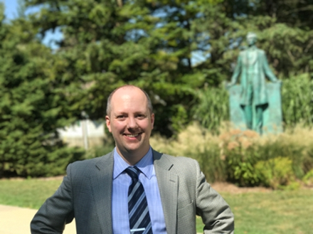 Photo of Erik Alexander standing in front of a statue outside on a sunny day