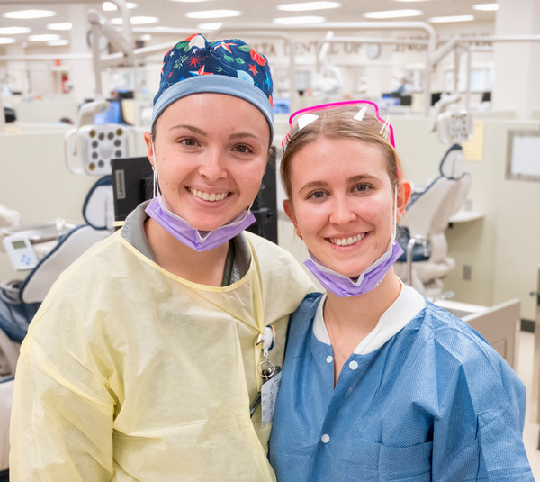 Two dentists dressed in clinic wear pose for camera