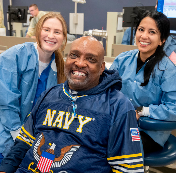 Veteran with NAVY jersey on poses in dental chair with two dentists
