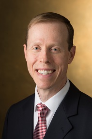 Head-and-shoulders professional portrait of a man in a suit against a neutral background.