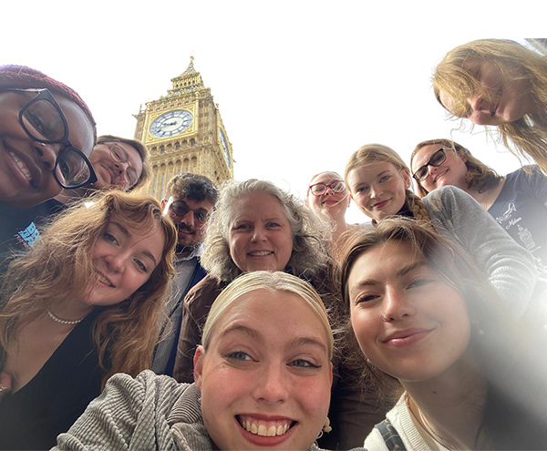 Group of students and professor look down at camera with London tower in the background