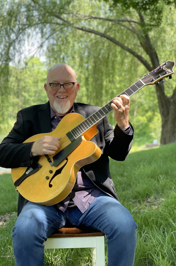 Rick Haydon with his guitar posed under a tree