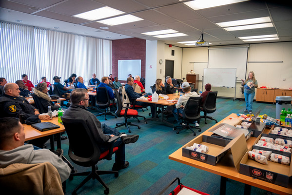 Attendees of diverse ages and backgrounds gather inside the Morris University Center for the Illinois Veterans Lunch, with boxed meals set out on tables during a presentation.