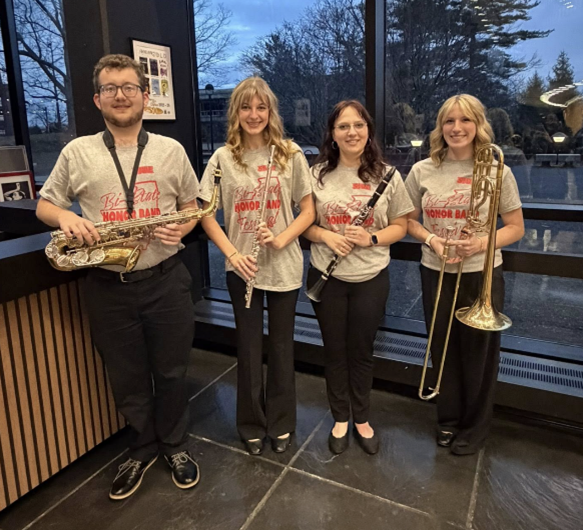 Four high school musicians wearing Bi-State Honor Band T-shirts stand indoors holding their instruments—alto saxophone, flute, clarinet and trombone—during the SIUE Bi-State Band event.