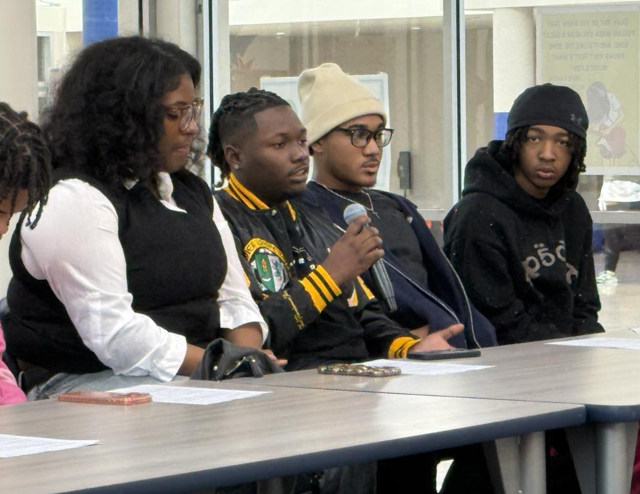 East St. Louis alumni participate in a panel discussion at a table, with one speaker holding a microphone while others listen beside him.