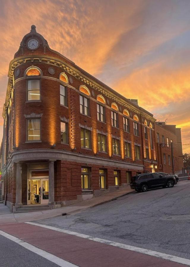 The Wedge Powered by SIUE, a historic red-brick corner building with arched windows and a clock tower, illuminated at sunset along a sloping street.