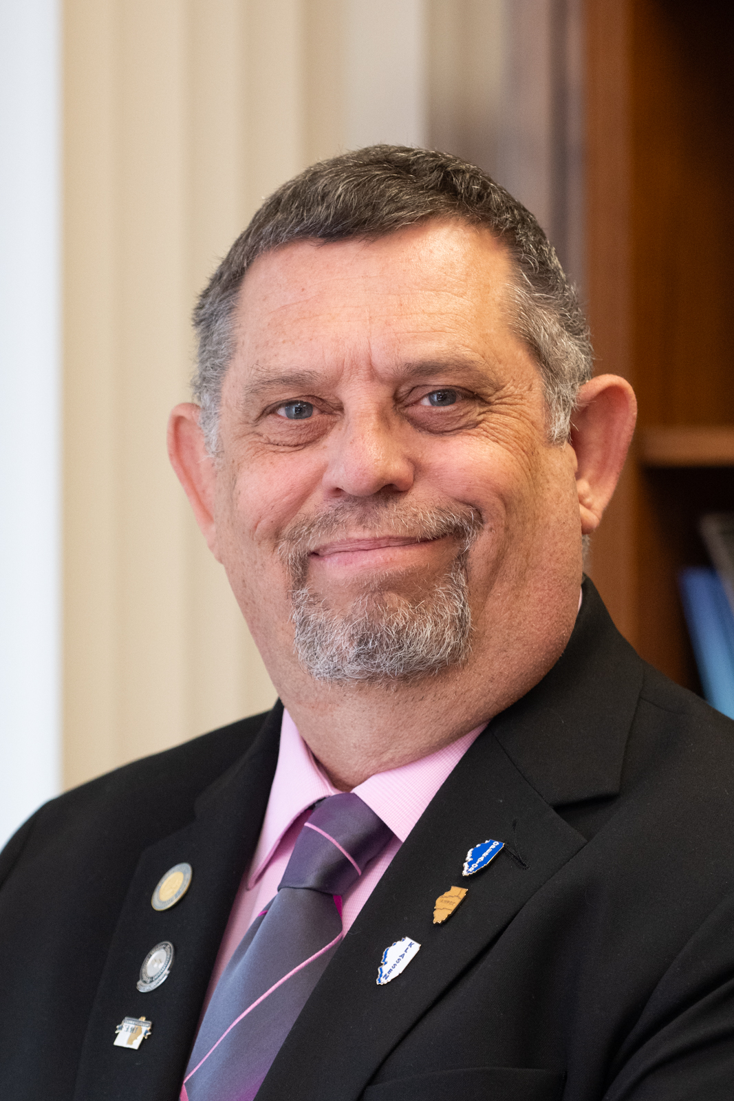 Portrait of Ricky Lallish, wearing a suit and lapel pins showing professional accomplishments