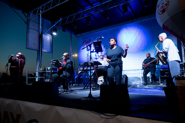 Charles Glenn Band on stage at One Day One SIUE at night, with blue spotlights flanking the stage and two women singing at a microphone