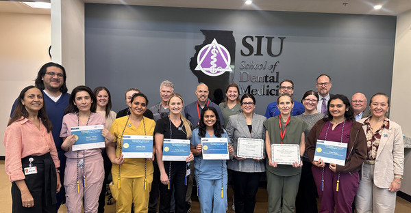 Group photo of student graduates holding certificates and their faculty