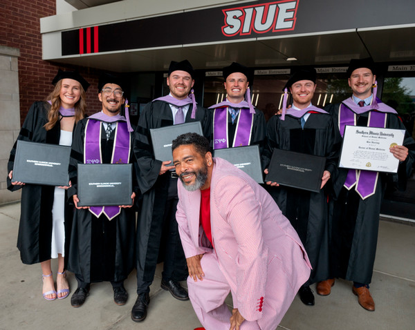 Chris Flamer poses in front of six dental graduates in their regalia