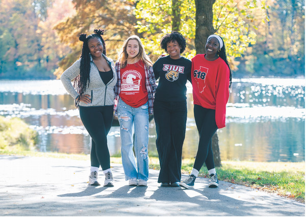Four young women on campus posing for camera under trees