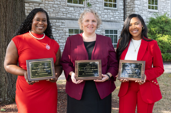 Three awardees stand outside under tree holding plaques at SIU School of Dental Medicine