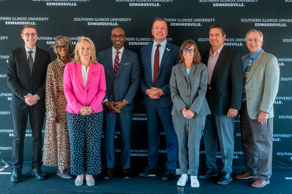 Photo of Chancellor Minor with a student researcher and members of the Illinois legislature in front of an SIUE sign