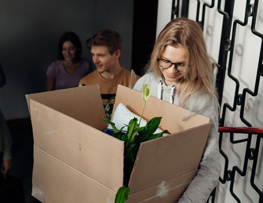 A student carrying a plant in a box. 